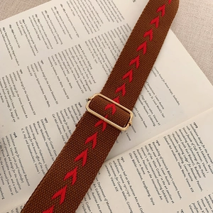 Vintage Umhängetasche mit breitem Pfeilmuster-Gurt und goldenen Schnallen auf Buchhintergrund