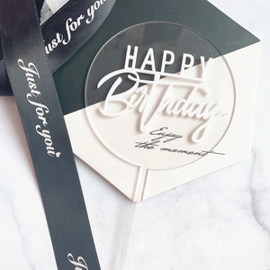 Clear acrylic round Happy Birthday cake topper with white lettering on marble surface