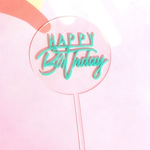 Clear acrylic round cake topper with green Happy Birthday 3D lettering on pink background