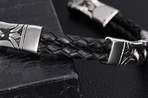 Macro shot of men's braided black leather bracelet with engraved silver metal totem details