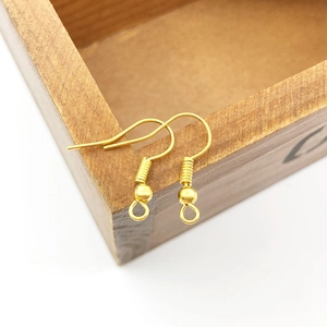 Macro shot of gold DIY earring hooks with bead and spring detail on wood box edge