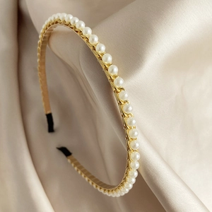 Detail van een vintage gouden haarband met elegante parels op een crème satijnen stof