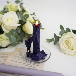 Elegant purple dripping pillar candle with glass base and vintage floral background