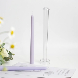 Tall tapered candle and clear plastic mold with base set on a minimalist white table