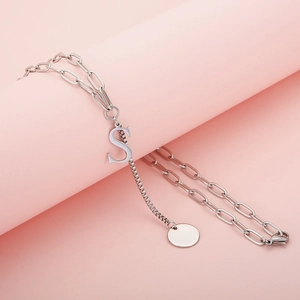 Elegant silver letter S pendant necklace displayed on a soft pink cylindrical jewelry stand