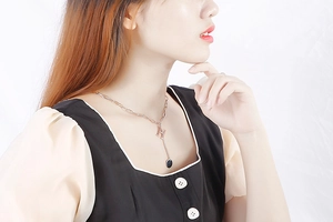 Close-up of rose gold H letter pendant necklace with black circular charm on model