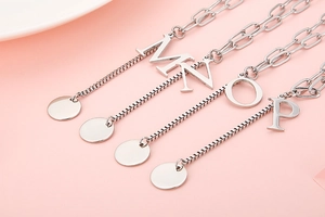 Detail of silver letter pendants M N O P on a delicate chain over pink background