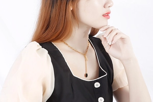 Detail of a gold Y-shaped necklace with paperclip chain and black circular pendant