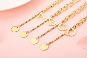 Detailed view of golden paperclip and box chain necklaces featuring letters A, B, C, D