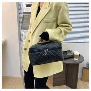 Detail of black quilted makeup bag with handle and silver zippers held by model