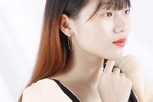 Close-up of a silver wavy large hoop earring worn by a model on white silk background