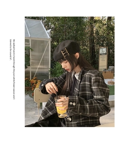 Close-up of black wool beret with gold metal pin detail worn with plaid blazer