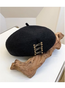 Detail shot of a black wool beret featuring a vintage metal buckle on a wooden stand