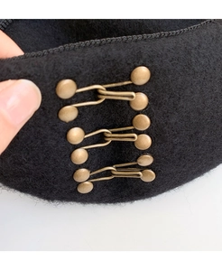 Detail of vintage bronze metal buckles on high-quality black wool fabric beret