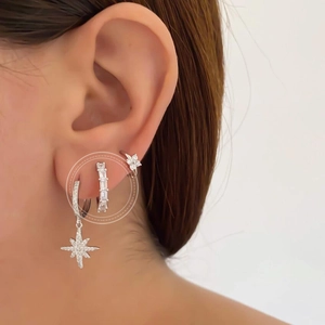 Detail of silver hoop earrings with cubic zirconia and star charms worn on ear