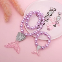 Detailed view of girls mermaid jewelry set with purple pearls on a pink background