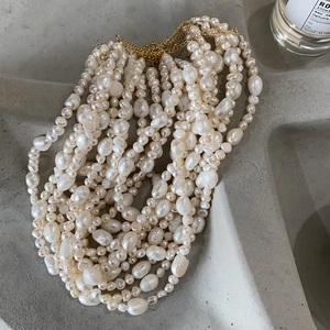 Detail of baroque pearl necklace with golden metal chains on a grey cement tray