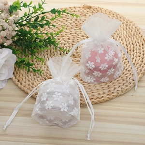 Detail view of floral printed organza drawstring pouches on a woven mat for gift storage