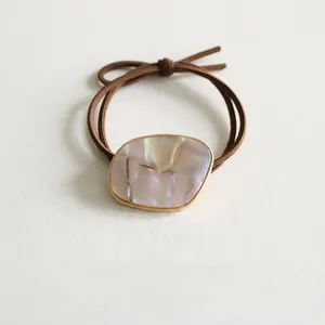 Detail of dark brown elastic hair tie with iridescent shell charm and gold metal rim