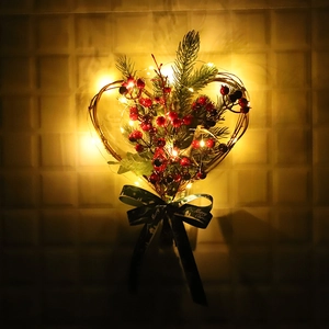 Heart-shaped Christmas wreath with red berries, pine needles and LED lights on a wall