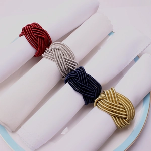 Detail of colorful woven rope napkin rings in red, silver, blue, and gold on white linens