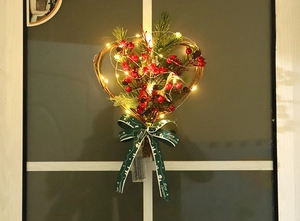 Close-up of heart-shaped Christmas wreath with red berries and LED lights on window