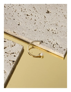 Macro view of C-shaped golden pearl ring featuring polished metal and soft reflection