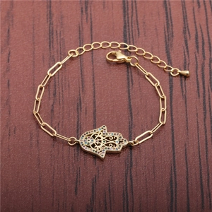 Gold Hamsa hand bracelet with multi-color zircons on a rustic wood background