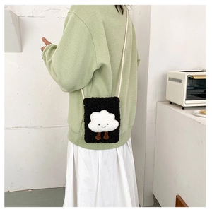 Close-up of black plush crossbody bag with white cloud motif worn on a female model