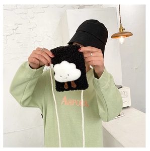 Close-up of plush black crossbody bag with white cloud smiley detail held by a model
