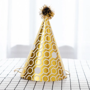 Golden honeycomb pattern party hat with plush pompom on checkered tablecloth decoration