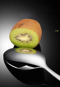 Macro view of mirror-polished stainless steel spoon reflecting fresh kiwi fruit