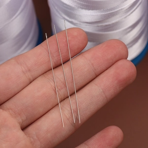 Three PONY silver stainless steel beading needles held over white ribbon for DIY sewing