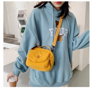 Girl wearing a cute yellow fuzzy lamb wool crossbody bag with bear embroidery over a blue hoodie