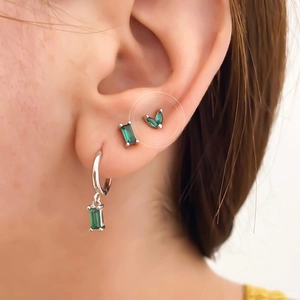 Marquise cut emerald green stud earrings set in silver finish on a female model's ear