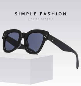 Close-up of black oversized sunglasses featuring silver three-dot rivet details on white stand