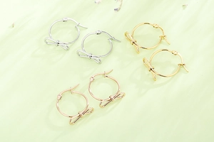 Trois paires de créoles avec nœud en argent, or et or rose sur un fond vert pastel