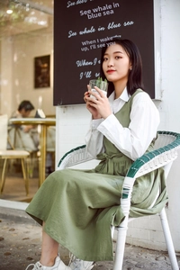 Detail of green cotton linen apron dress with adjustable waist tie and white shirt