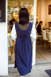 Detail view of the back of a navy cotton apron dress featuring an adjustable waist bow tie