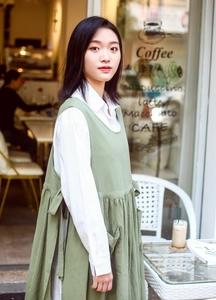 Macro detail of a green linen cotton pinafore apron worn by a model in a cafe setting