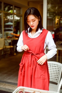 Detail of red cotton apron dress with side ties and large pockets in cafe setting