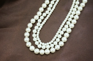 Close-up of triple-layered glass pearl necklace displayed on dark brown satin fabric