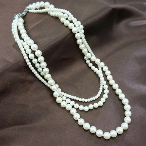 Elegant multi-layer white faux pearl necklace with silver clasp on brown silk fabric
