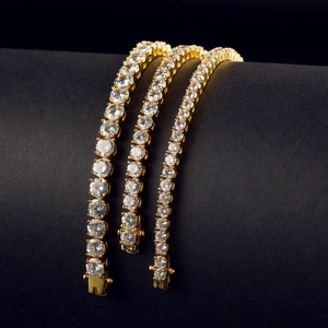 Three rows of gold plated tennis chains with white zircon stones on a dark background