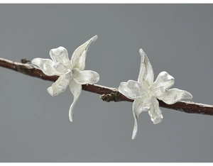 Macro shot of 3D matte silver iris earrings with textured petals on a branch