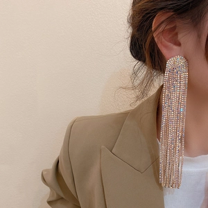 Close-up of sparkling rhinestone long tassel earrings worn by a model in a beige blazer