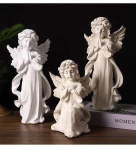Detailed view of three white resin praying angel figurines with classical wing details