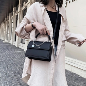 Minimalist black matte leather flap handbag with silver chain and crossbody strap shown on model