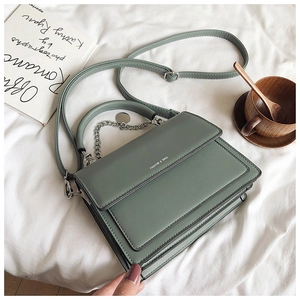 Detail of Morandi green flap bag with silver chain strap on white fabric background