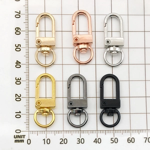 Six assorted metal swivel snap hooks in gold, silver, and black on a metric scale mat